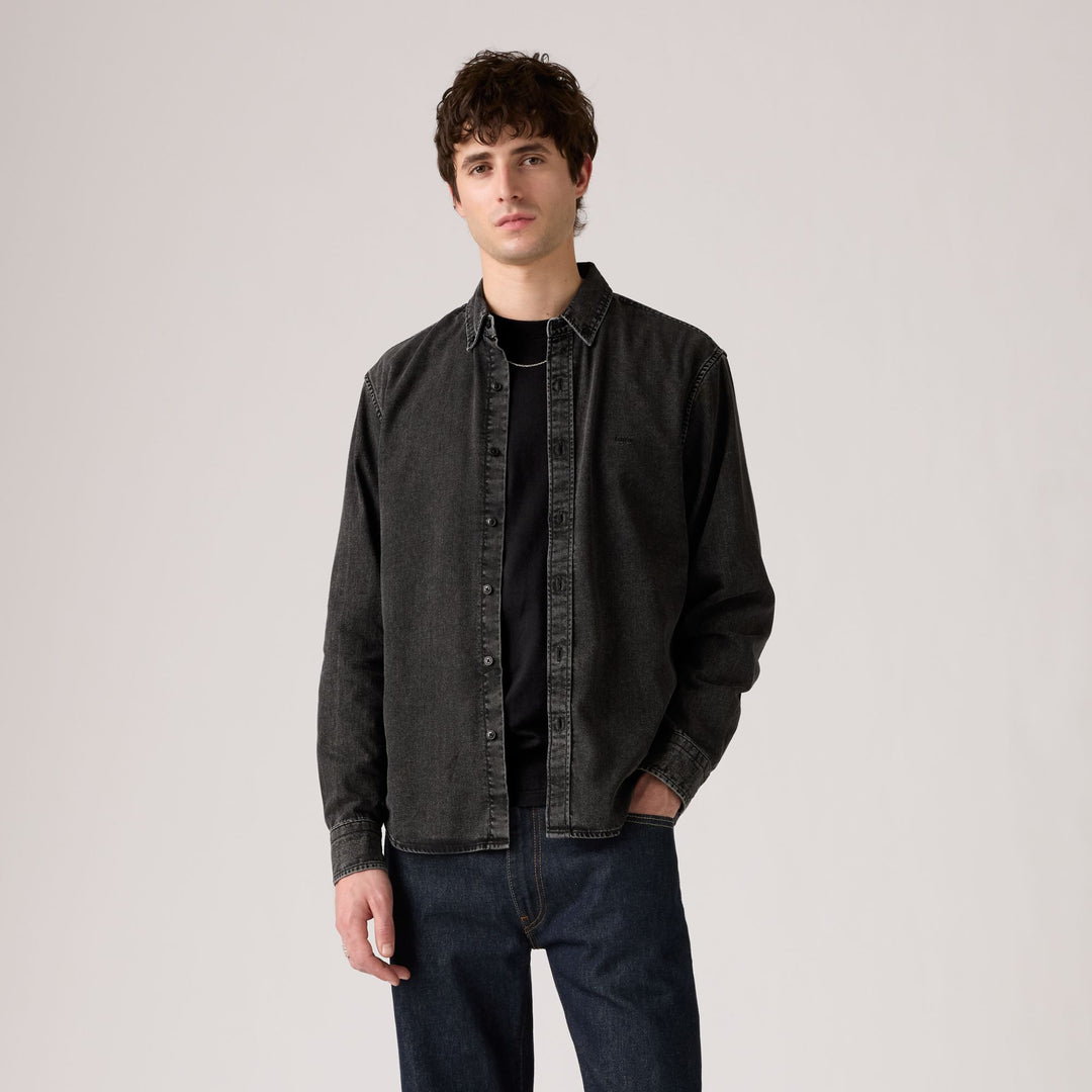 Man wearing a dark denim jacket over a black shirt on a plain background