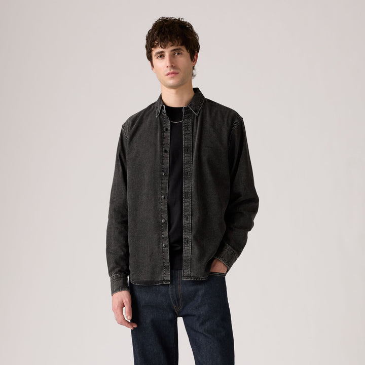 Man wearing a dark denim jacket over a black shirt on a plain background